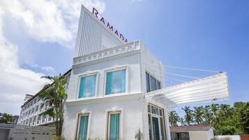 Un edificio moderno con un llamativo letrero 'RAMAD', ventanas amplias y un área exterior cubierta con plantas en macetas.