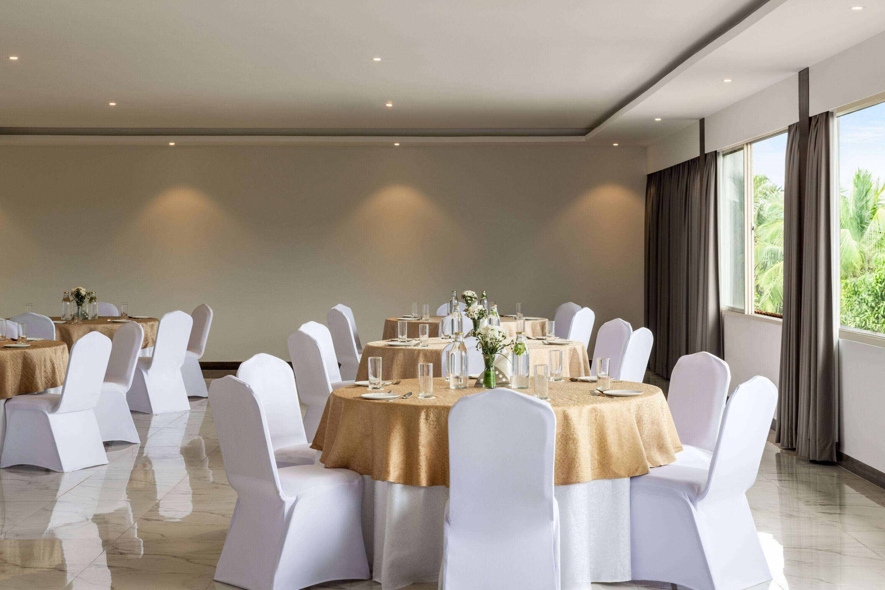 Un salón de conferencias con mesas redondas, sillas blancas y mantel dorado.