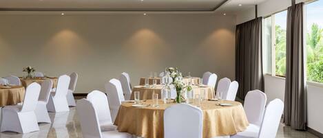 Un salón de conferencias con mesas redondas, sillas blancas y mantel dorado.