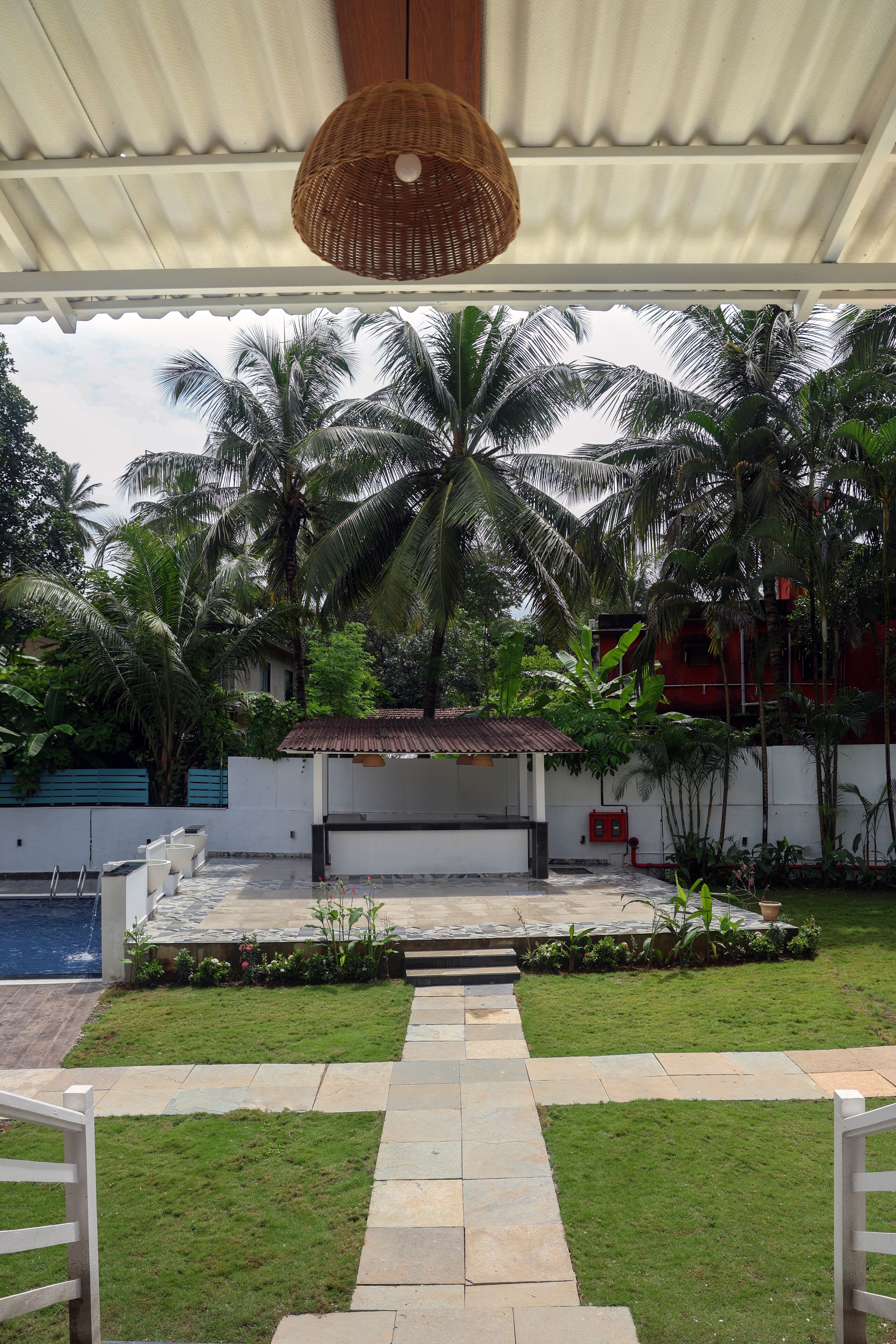 A covered outdoor area with a pathway leading to a seating area, surrounded by lush greenery and palm trees.