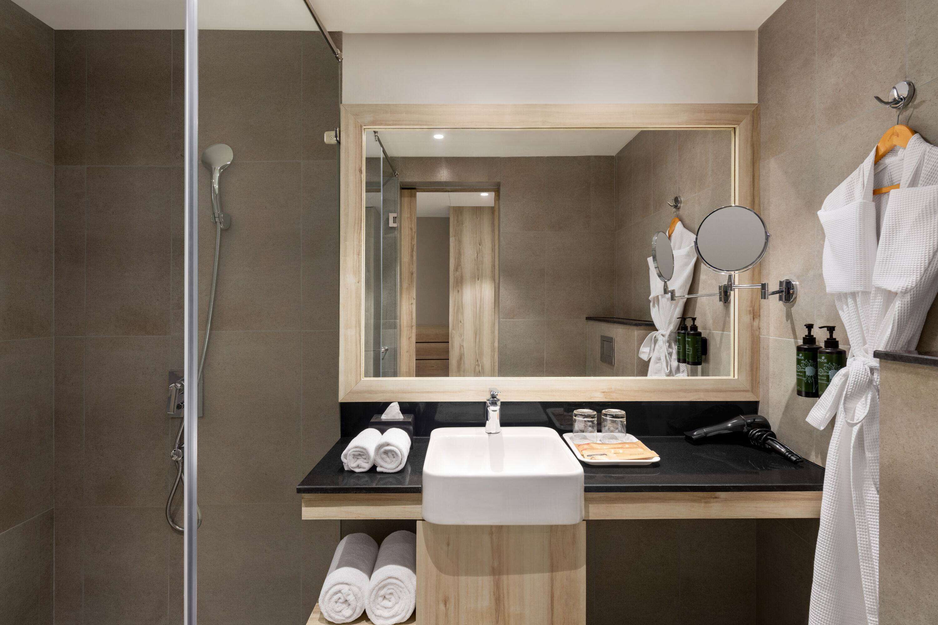 Un baño moderno con ducha, lavamanos y espejo. Hay toallas y artículos de aseo en la encimera.
