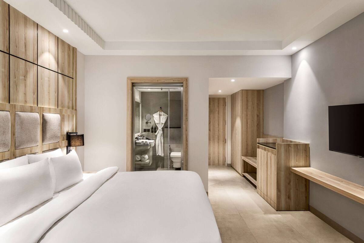 A modern hotel room with a large bed, wooden paneling, a TV, and a walk-in closet.