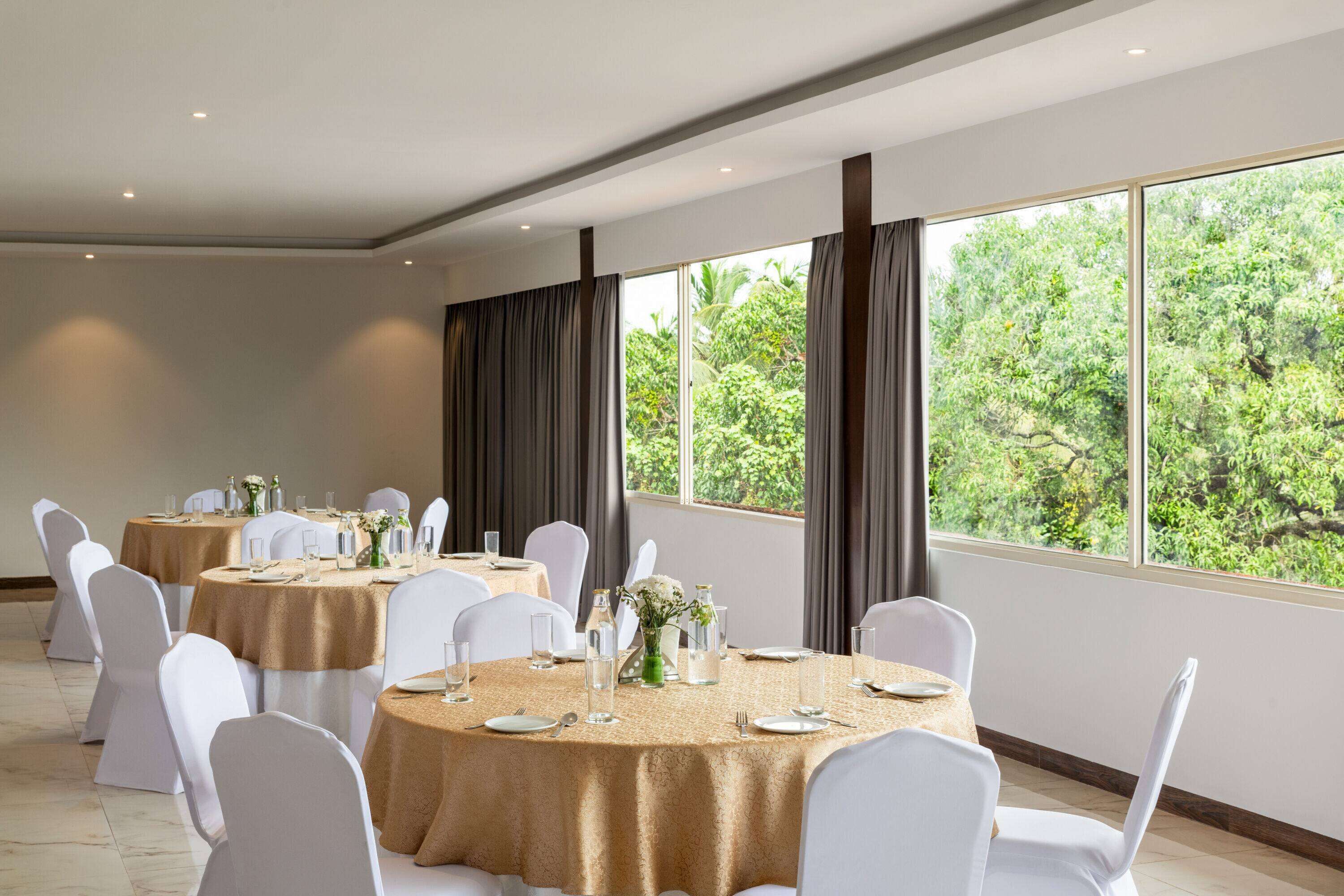 A conference room with round tables, white chairs, and large windows with curtains.