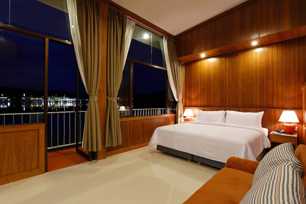 A hotel room with a large bed, a nightstand with a lamp, and a balcony with curtains.
