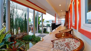 Un pasillo con suelo de madera, ventanas de marco rojo y plantas de interior.