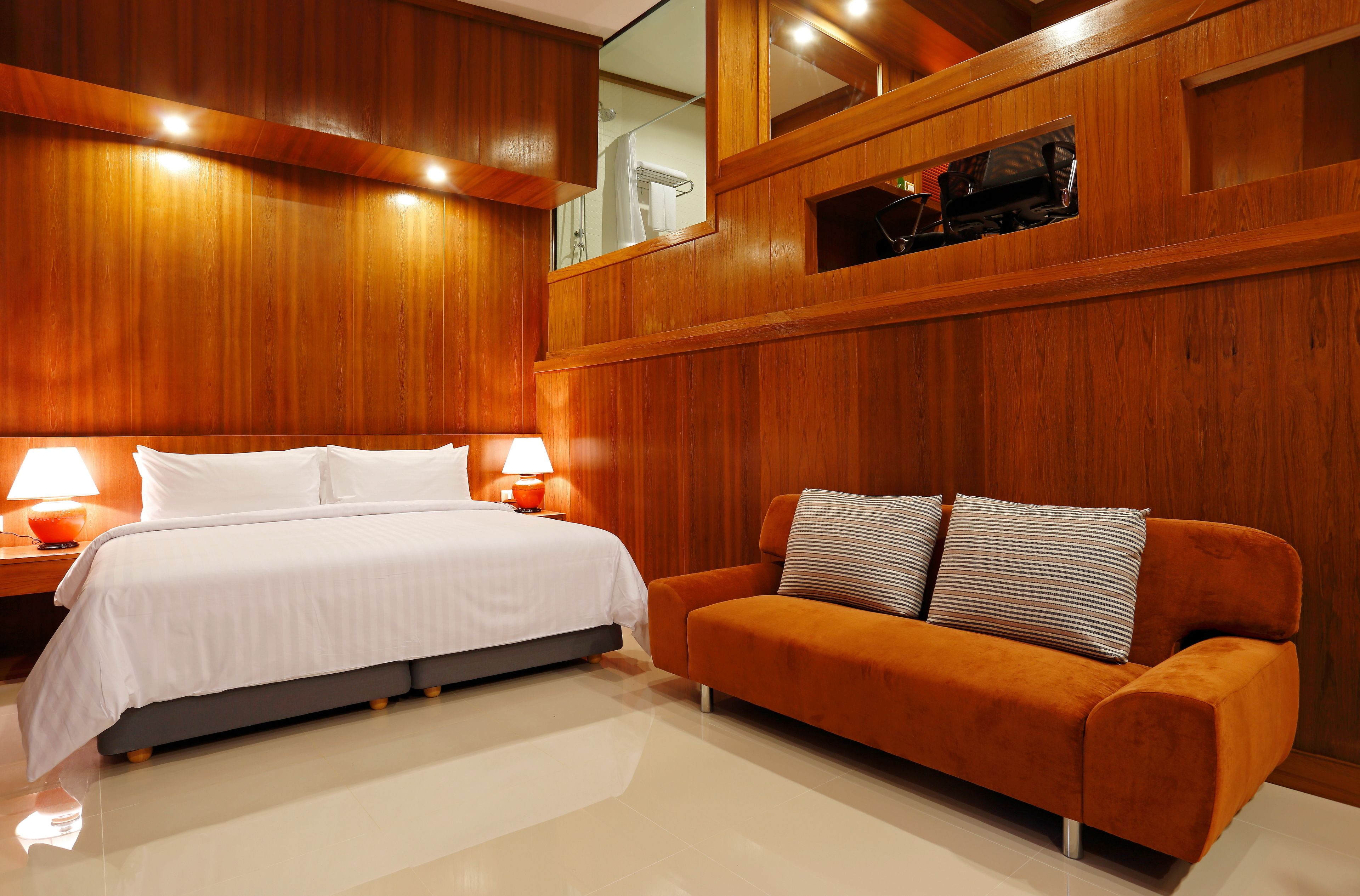 Una habitación de hotel moderna con una cama grande, un sofá, paneles de madera y una televisión.