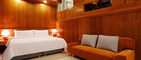 Una habitación de hotel moderna con una cama grande, un sofá, paneles de madera y una televisión.