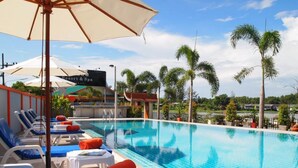 Una piscina con sillas de descanso y sombrillas, rodeada de palmeras y un edificio de resort al fondo.