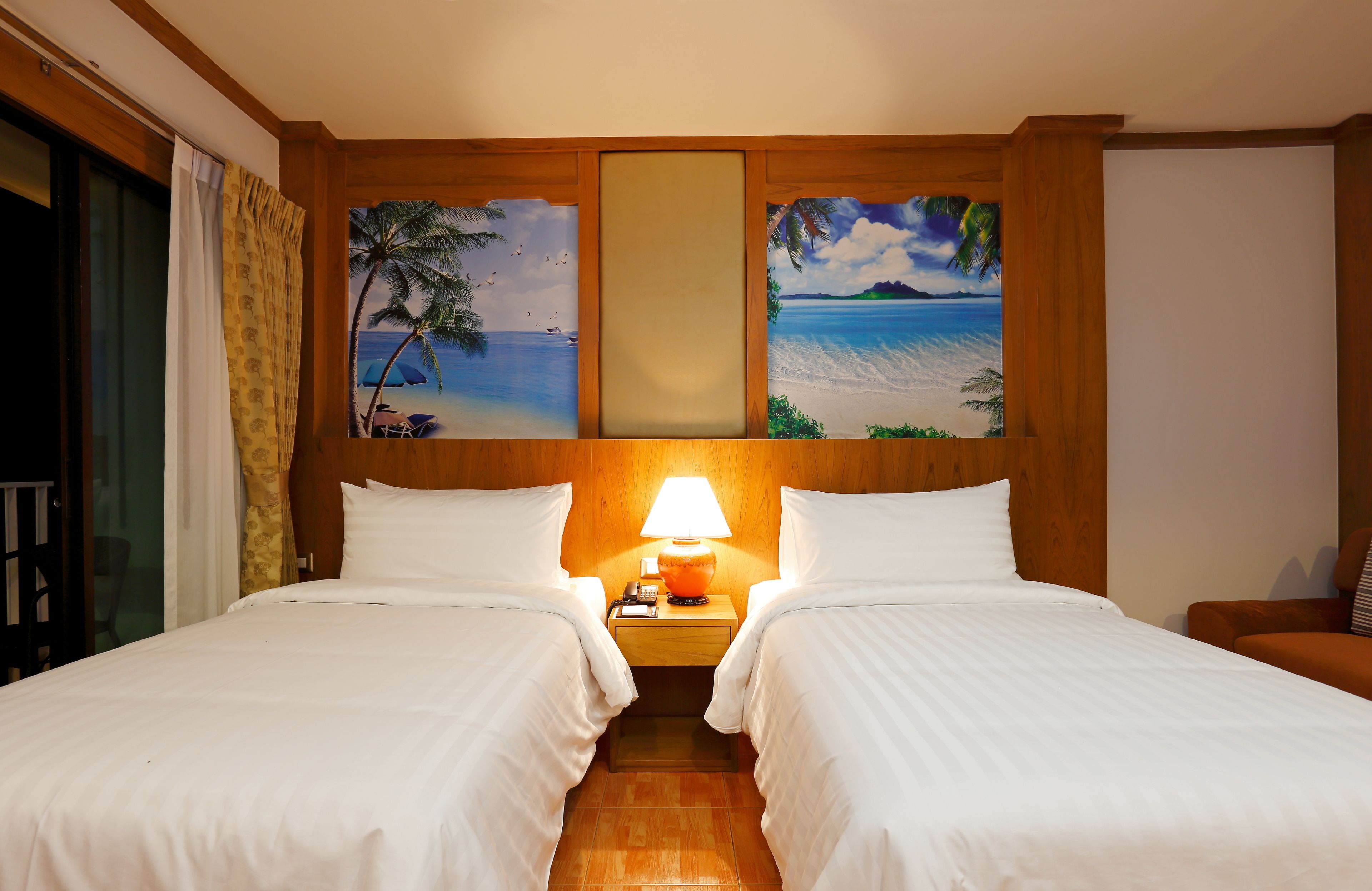 A hotel room with two beds, a nightstand with a lamp, and a painting of a beach scene on the wall.