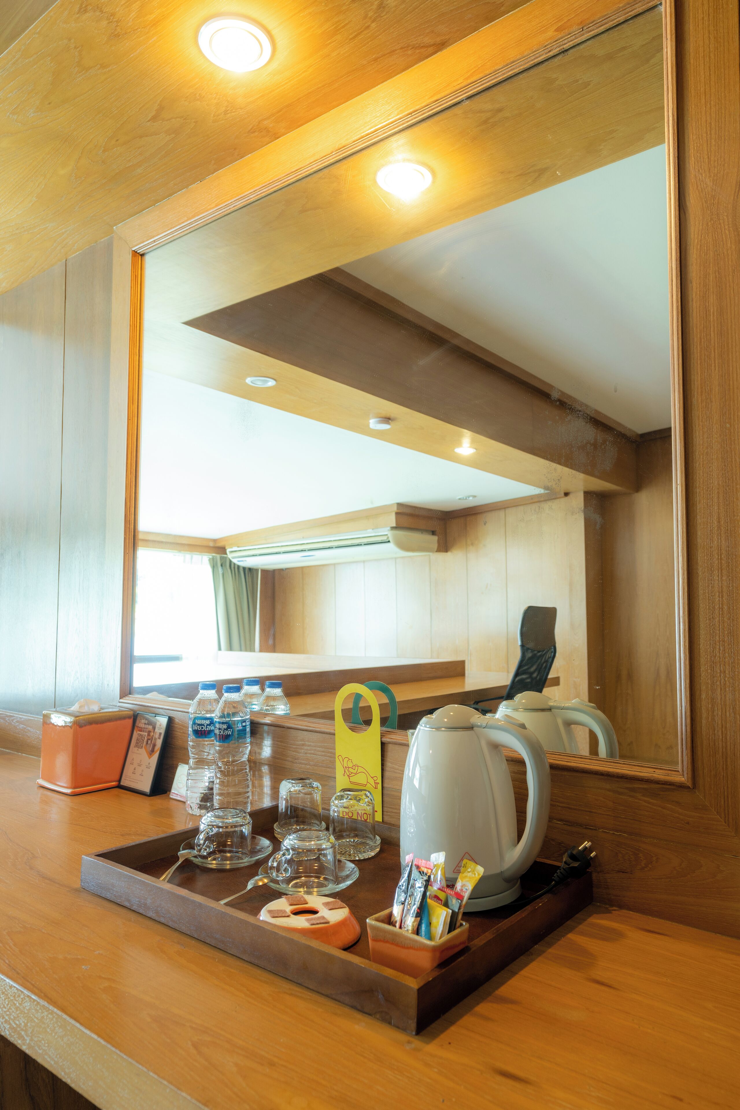 Habitación de hotel con mostrador de madera, una bandeja con vasos, tetera y una planta pequeña.