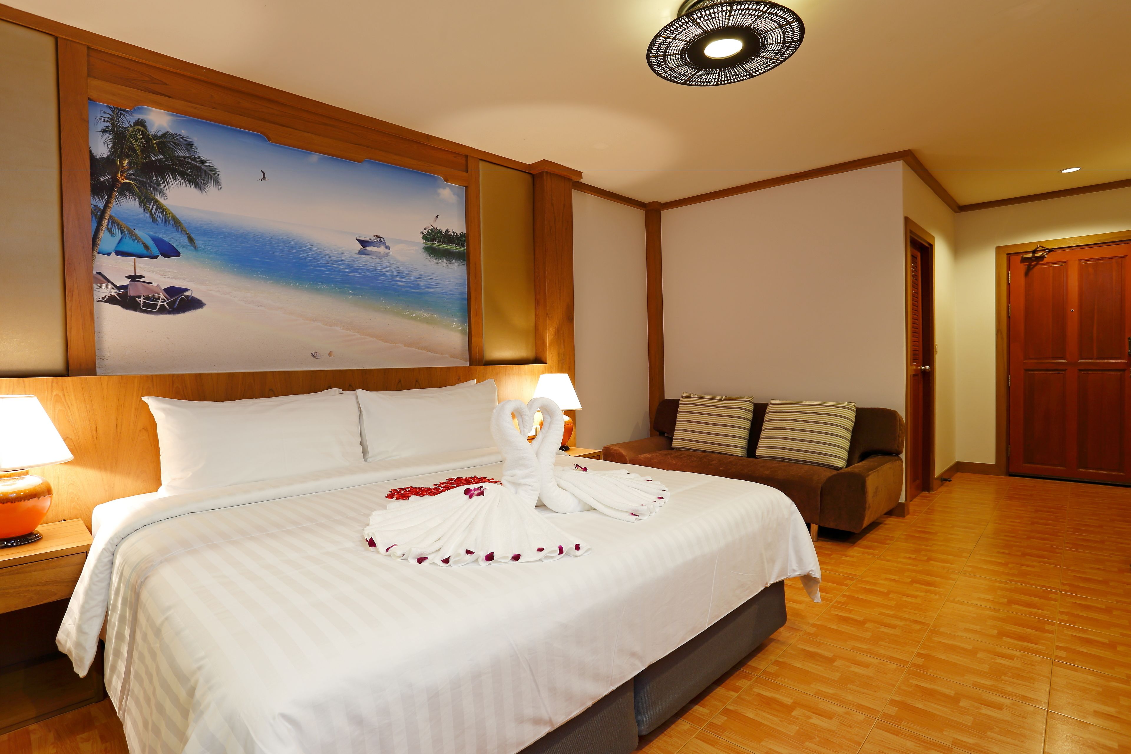 A hotel room with a large bed, a painting of a beach scene, a wooden floor, and a wooden door.