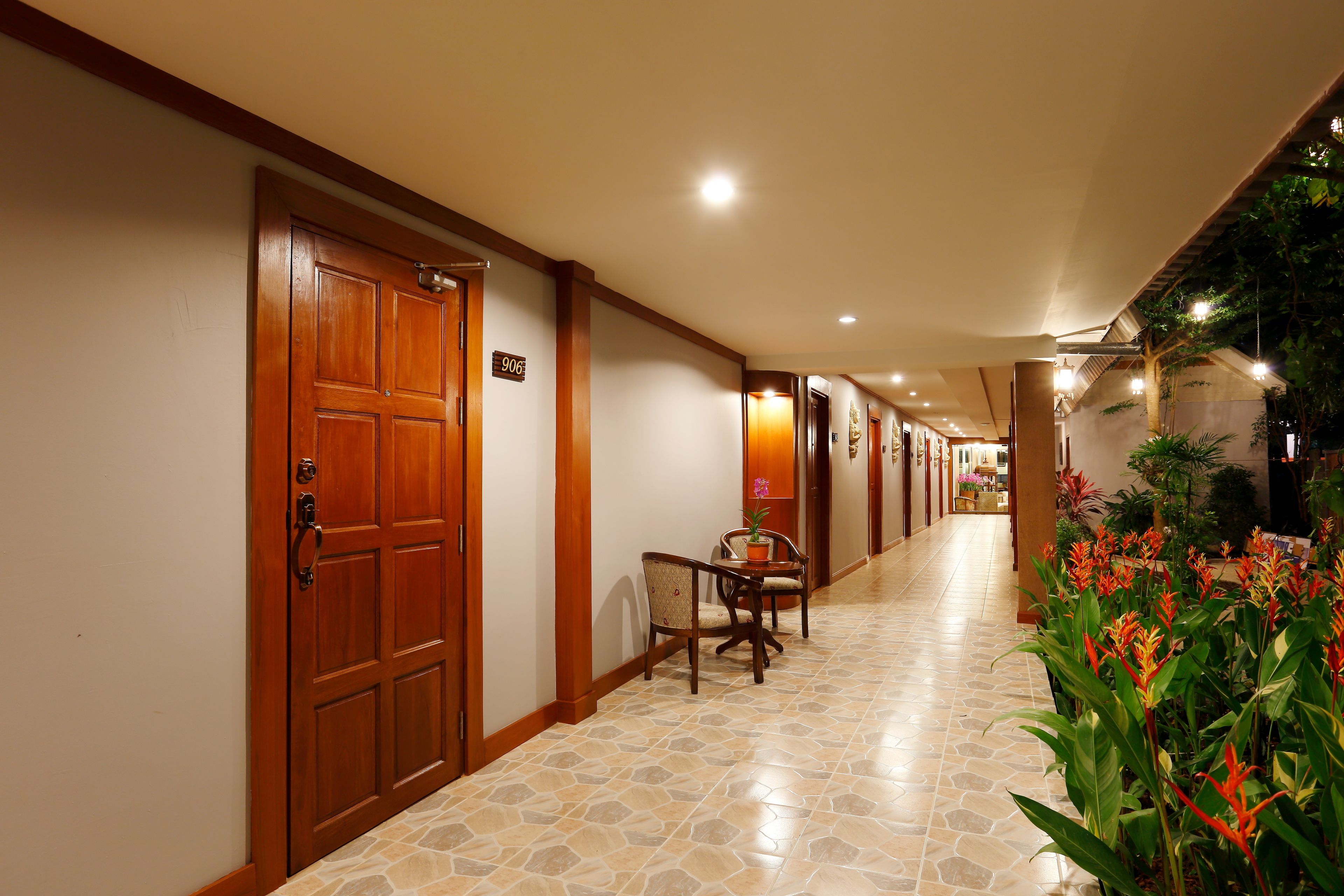 A hotel corridor with a wooden door, a seating area with a table and chairs, and a potted plant.