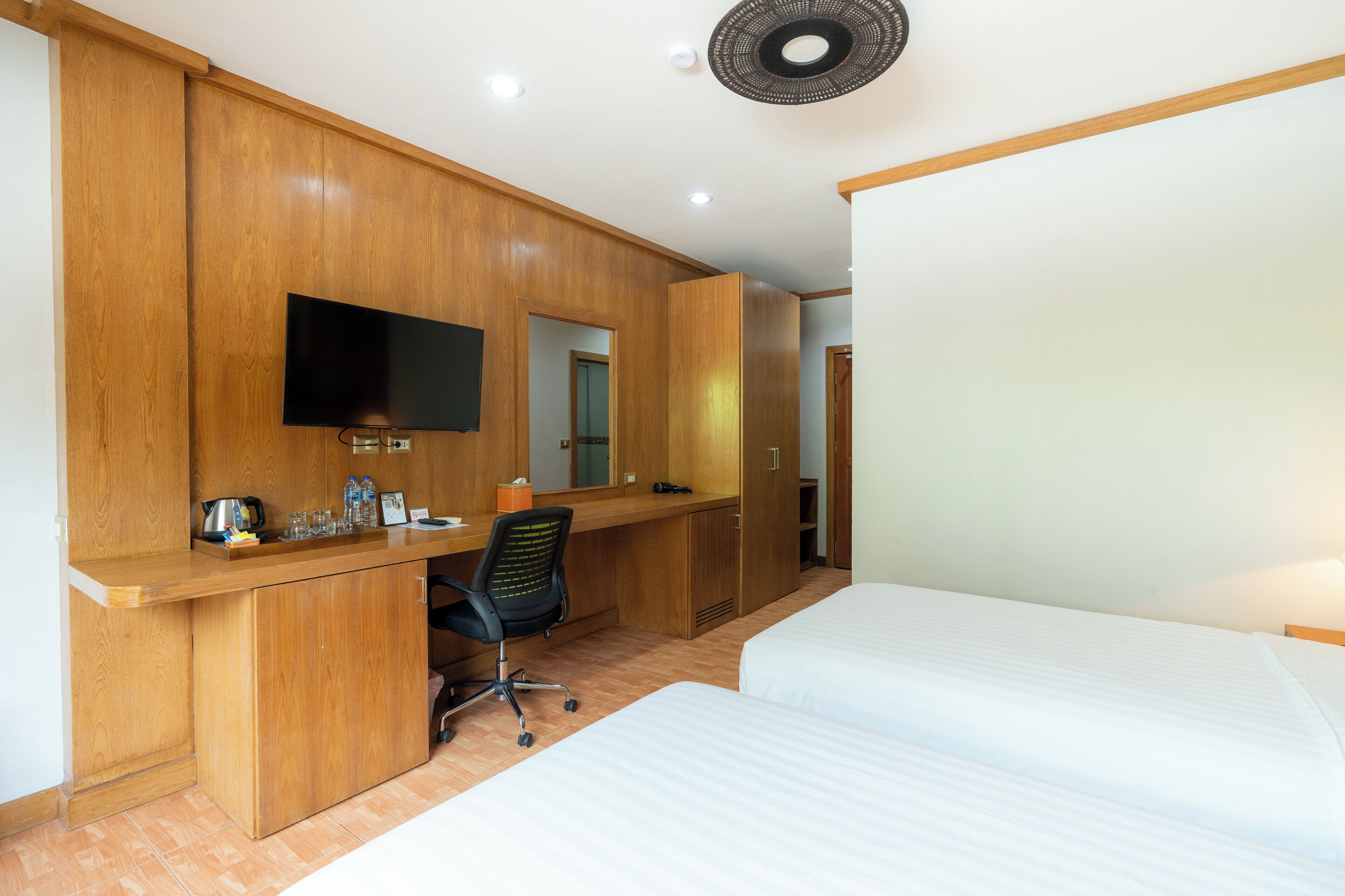 Habitación de hotel con un escritorio de madera, un televisor de pantalla plana, una silla y dos camas.