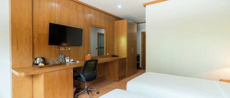 Habitación de hotel con un escritorio de madera, un televisor de pantalla plana, una silla y dos camas.