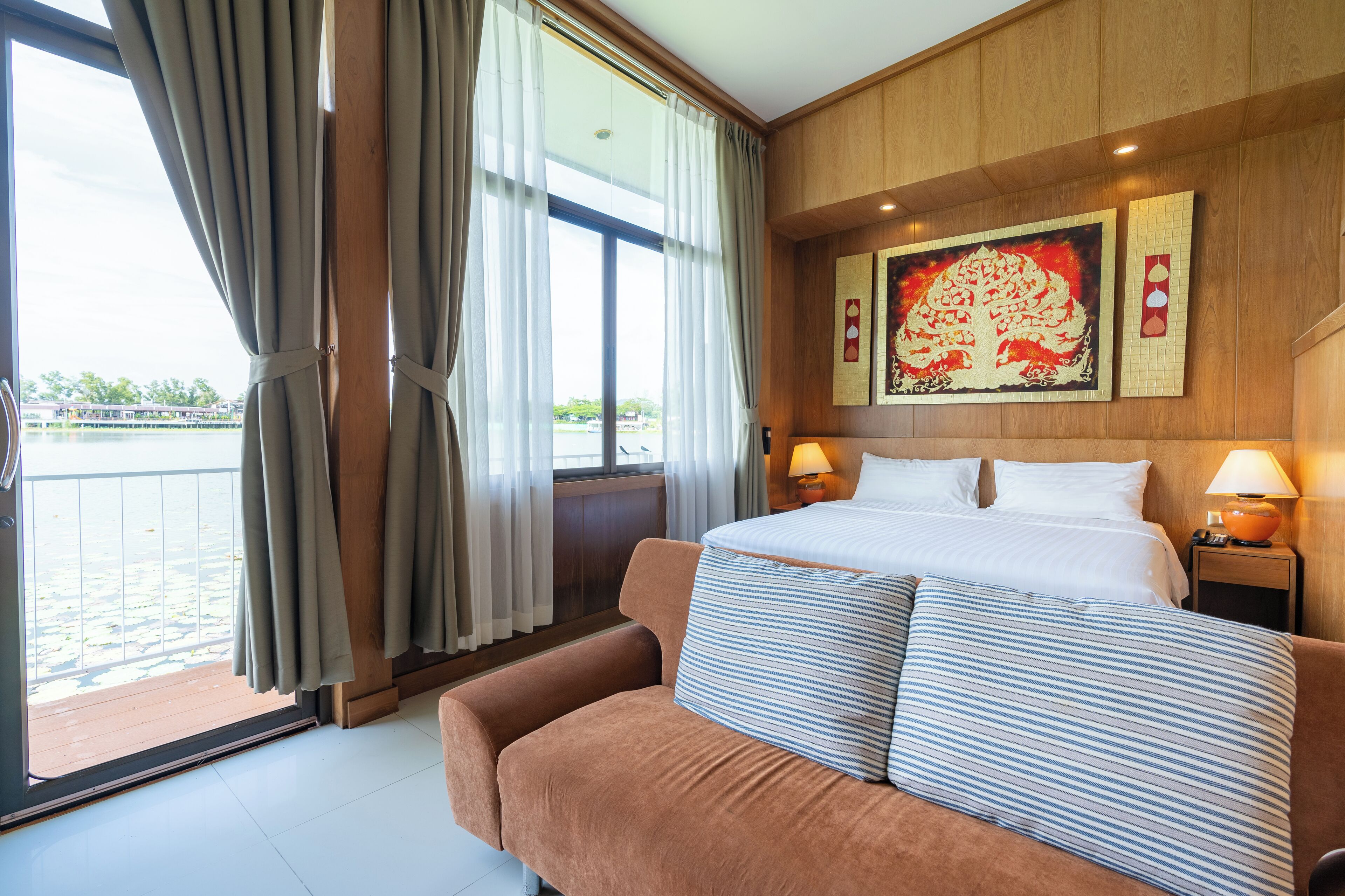 A hotel room with a bed, a sofa, a window with curtains, and a painting on the wall.