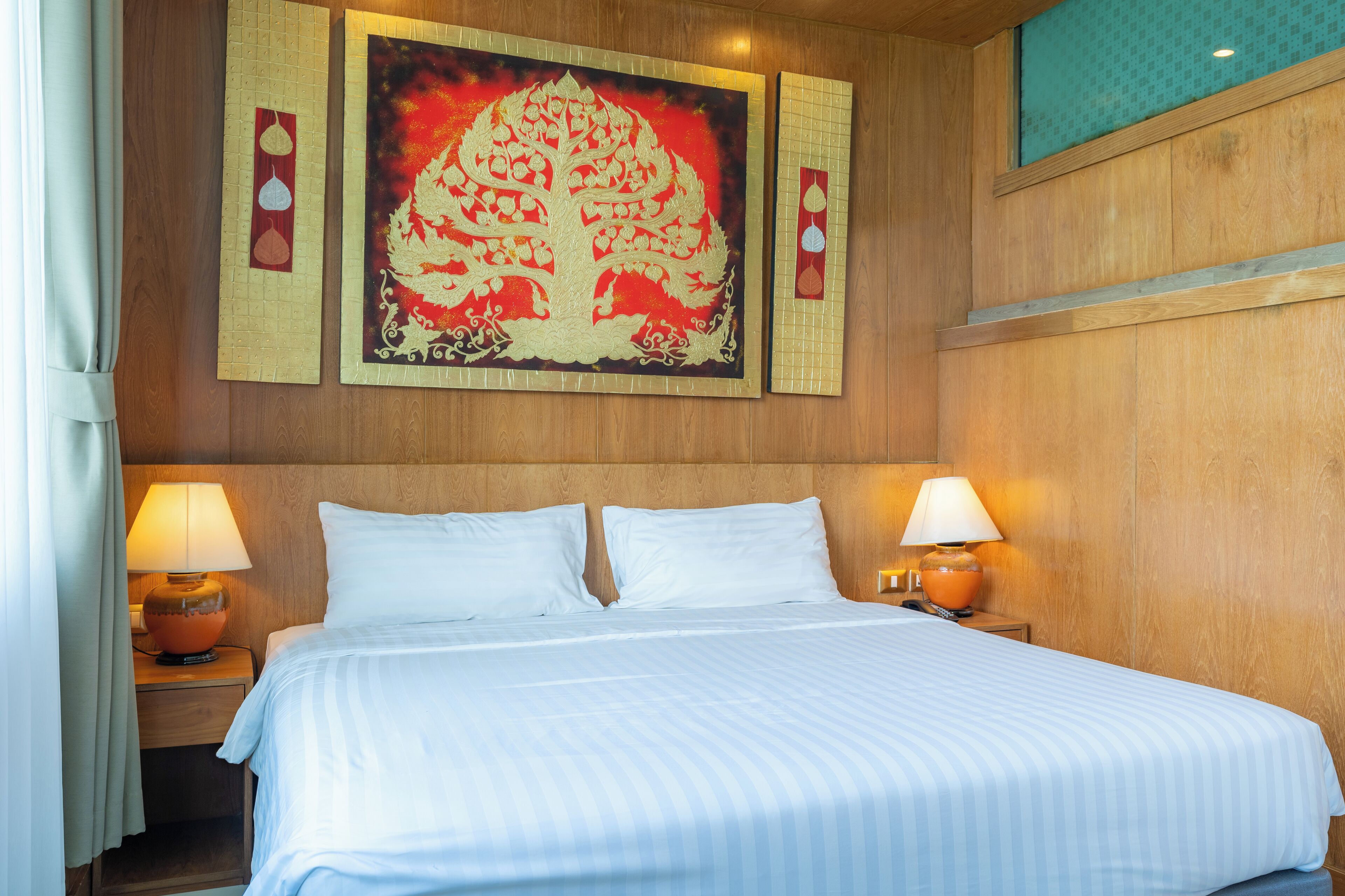 A hotel room with a large bed, two bedside lamps, and a wall with a decorative painting.