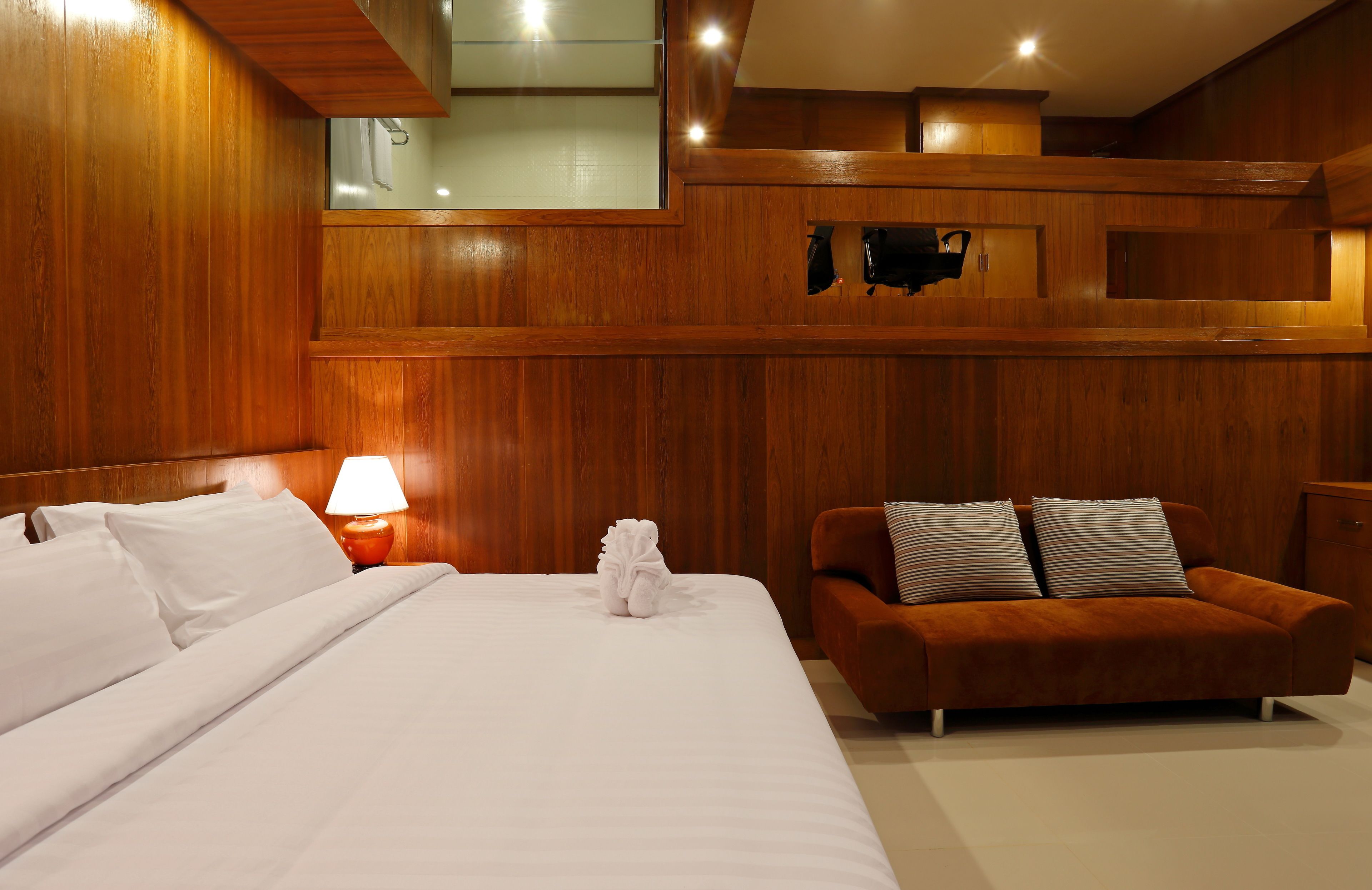 Una habitación de hotel con una cama grande, un sofá, una mesita de noche con lámpara y paneles de madera.