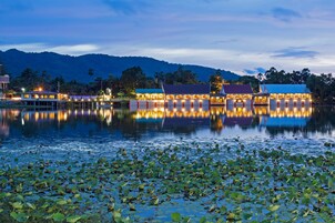 Un hotel frente al agua con varias edificaciones reflejadas en el agua, rodeado de hojas de loto.