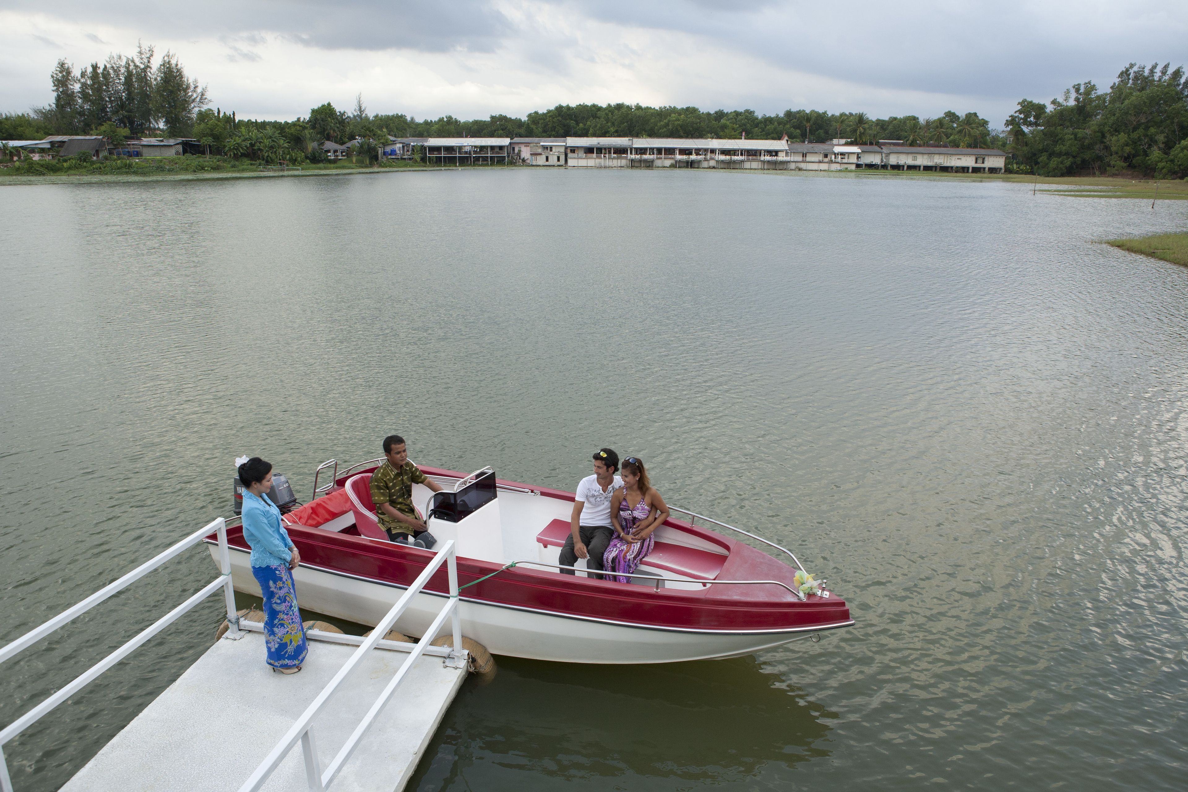 Un pequeño bote rojo y blanco amarrado en un muelle, con algunas personas de pie y sentadas.