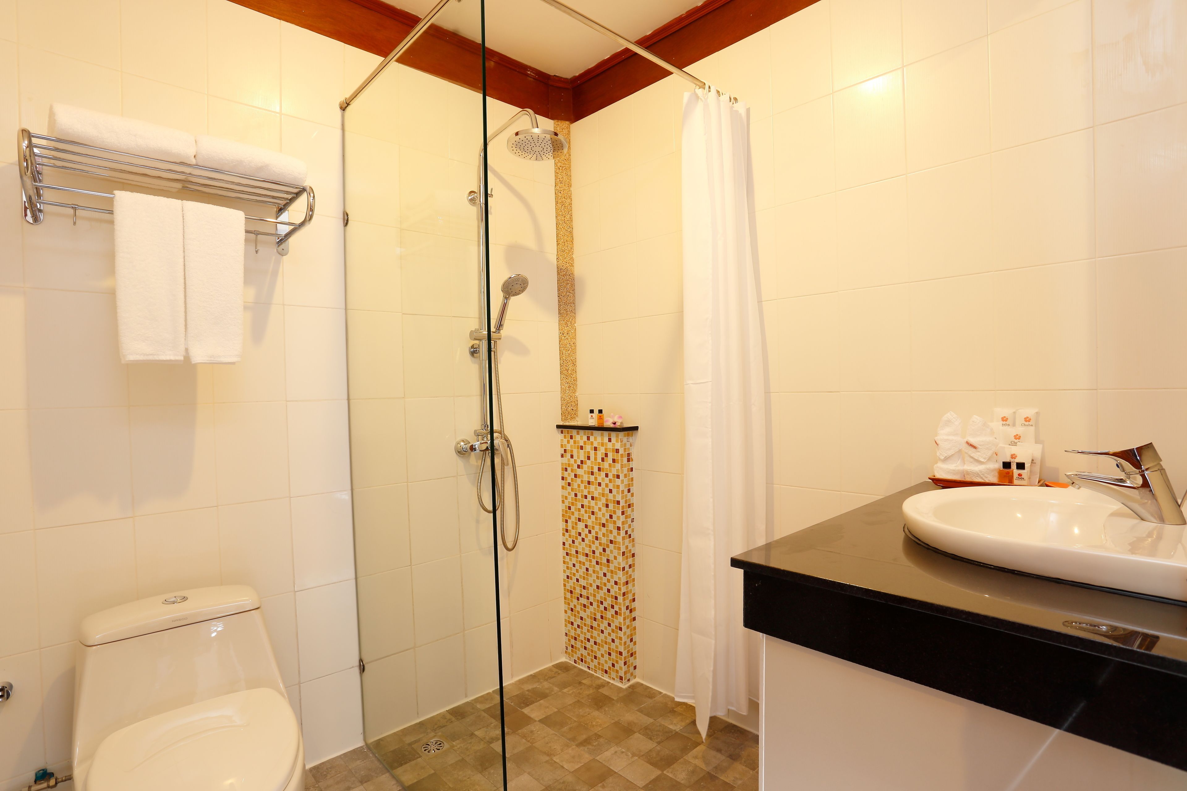 Baño con ducha envuelta en vidrio, inodoro blanco, lavabo con encimera negra y perchero con dos toallas.