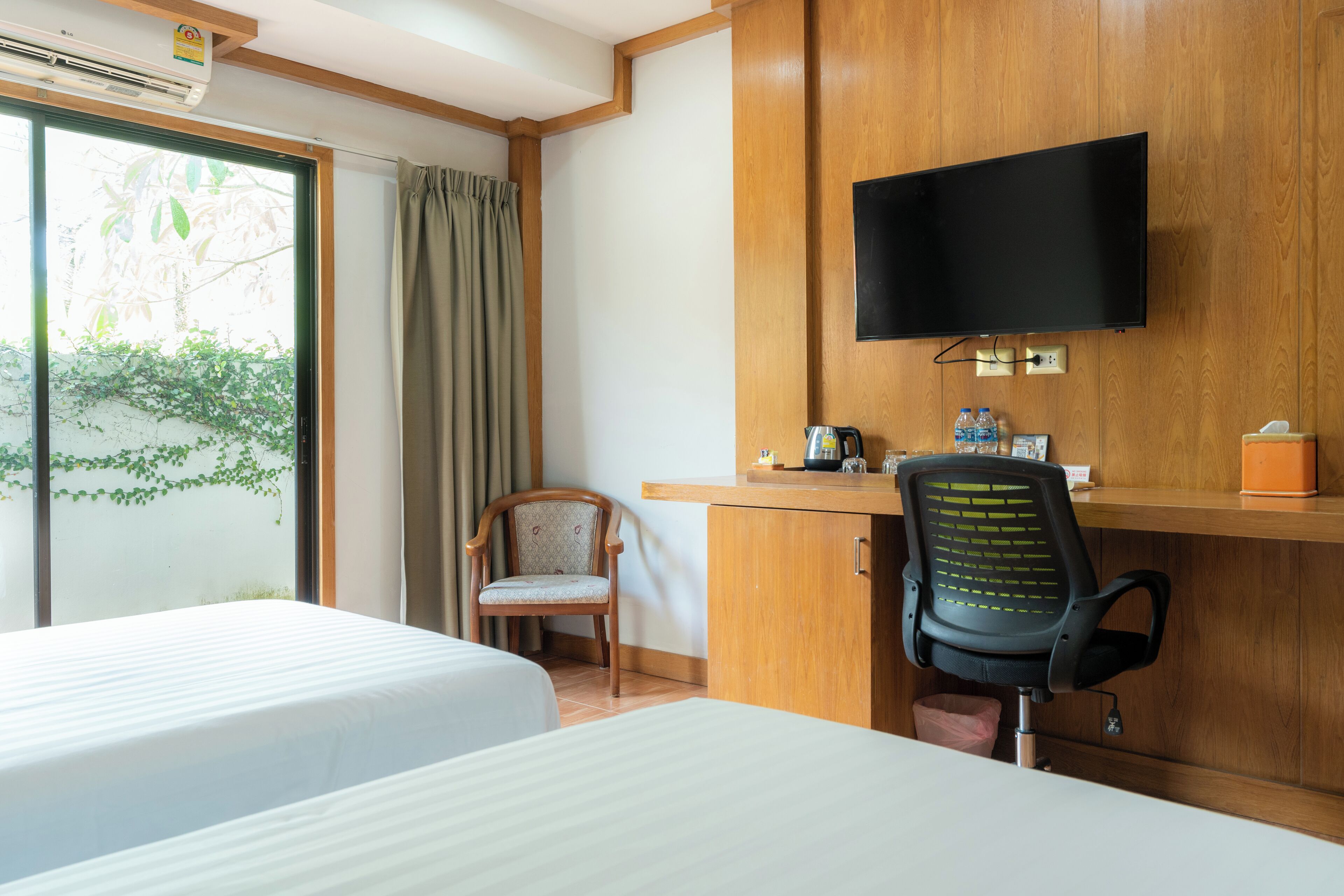 A hotel room with two beds, a wooden desk with a television, a chair, and a window with curtains.