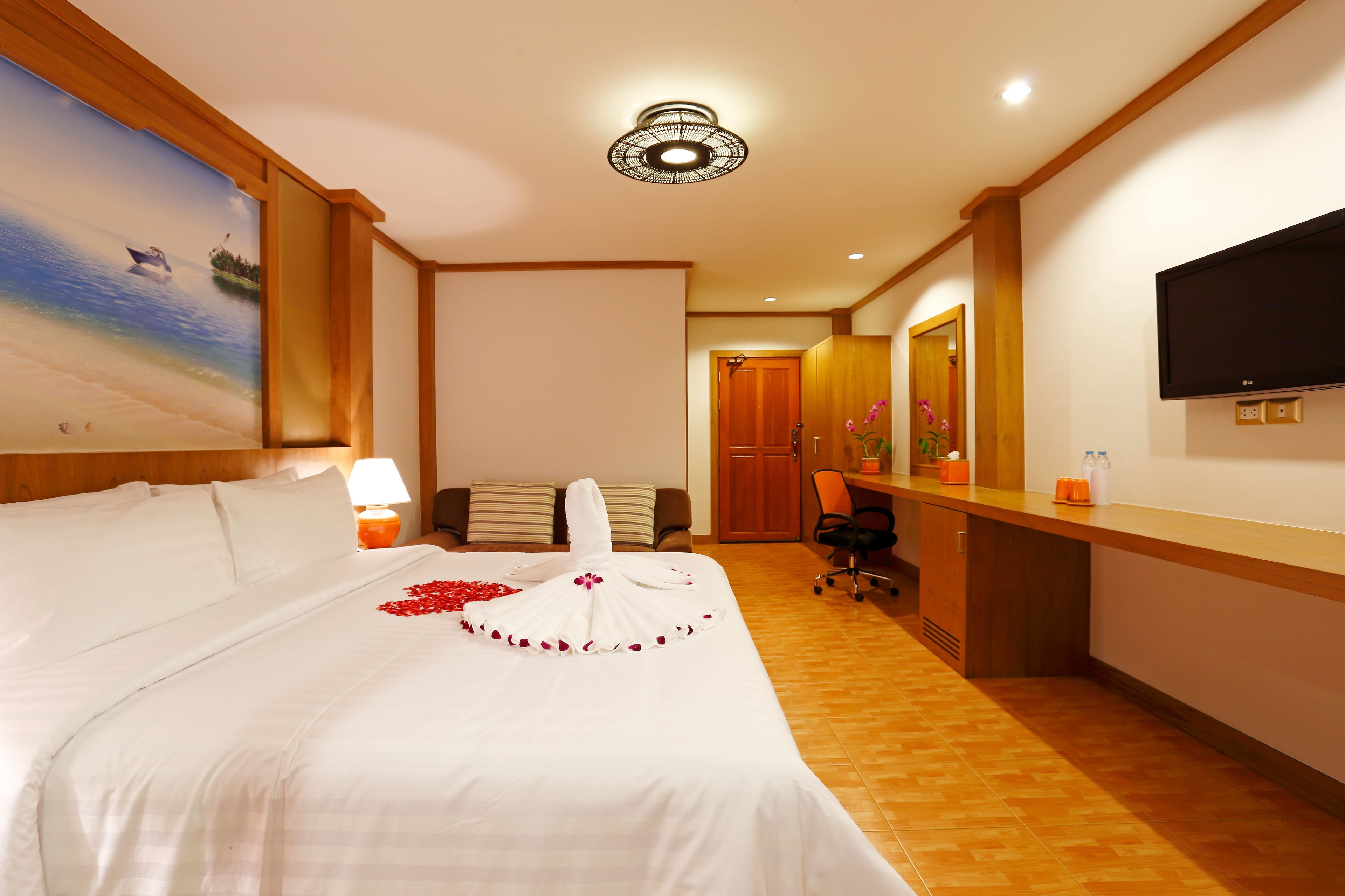 Habitación de hotel con una cama grande, un escritorio, un televisor y un cuadro de una playa.