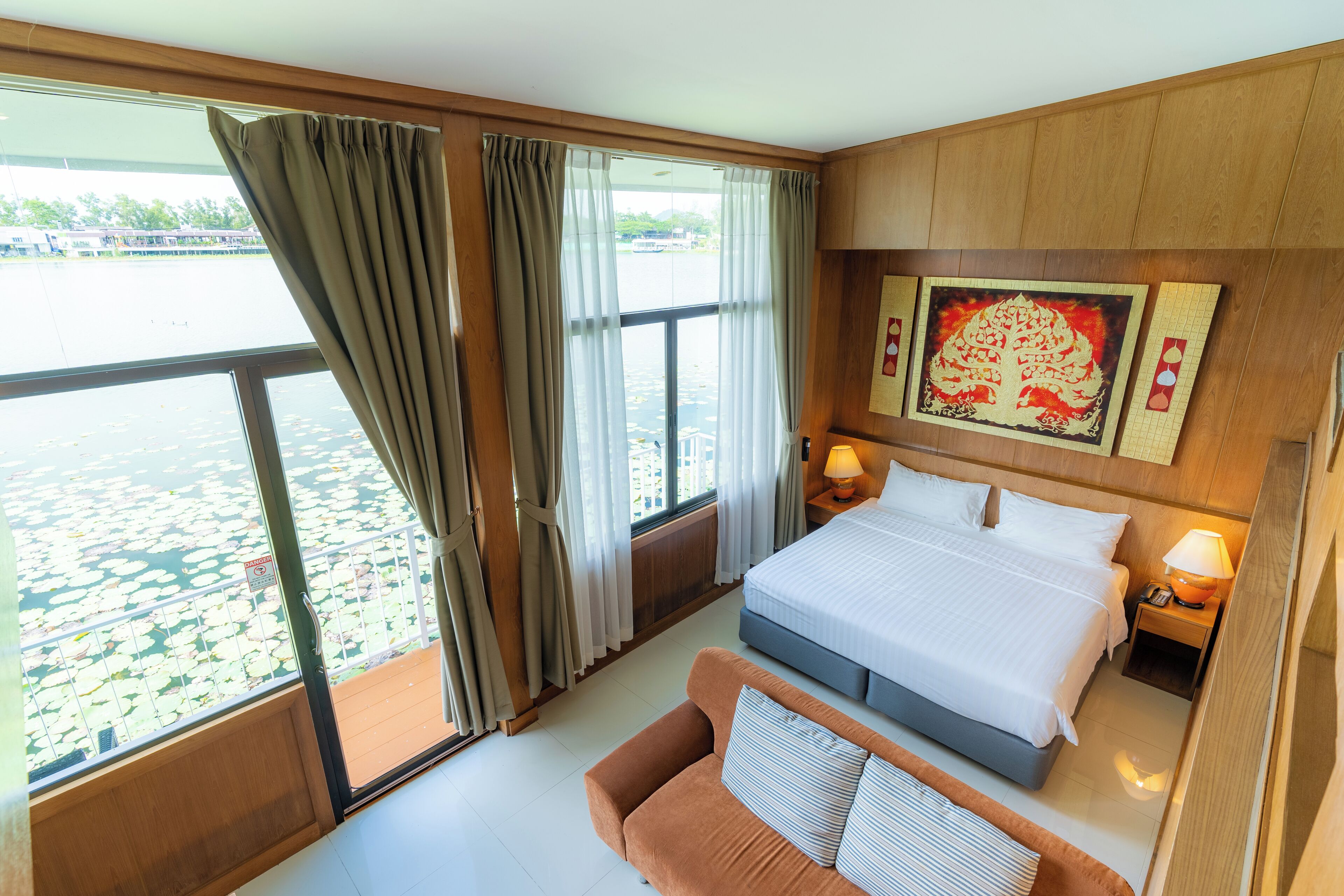 A hotel room with a large window, a bed, a sofa, and a nightstand with a lamp.