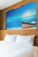 Habitación de hotel con cama, ropa de cama blanca, un cuadro grande de un bote en la playa y paneles de madera en las paredes.