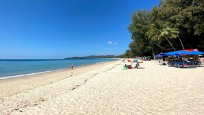 Una playa con cielos despejados, palmeras y sombrillas.