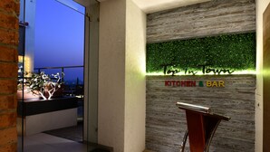 A modern interior with a glass wall leading to a balcony, a wooden wall with a green foliage design, and a sign reading "KITCHEN BAR". - Krishna Palace Hotel Ambernath (Ambernath)