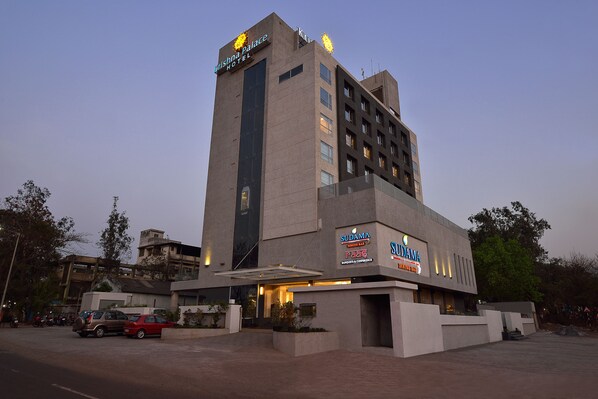 A hotel with a modern design, featuring a prominent sign for the Krishna Palace Hotel and Sudama Hotel.