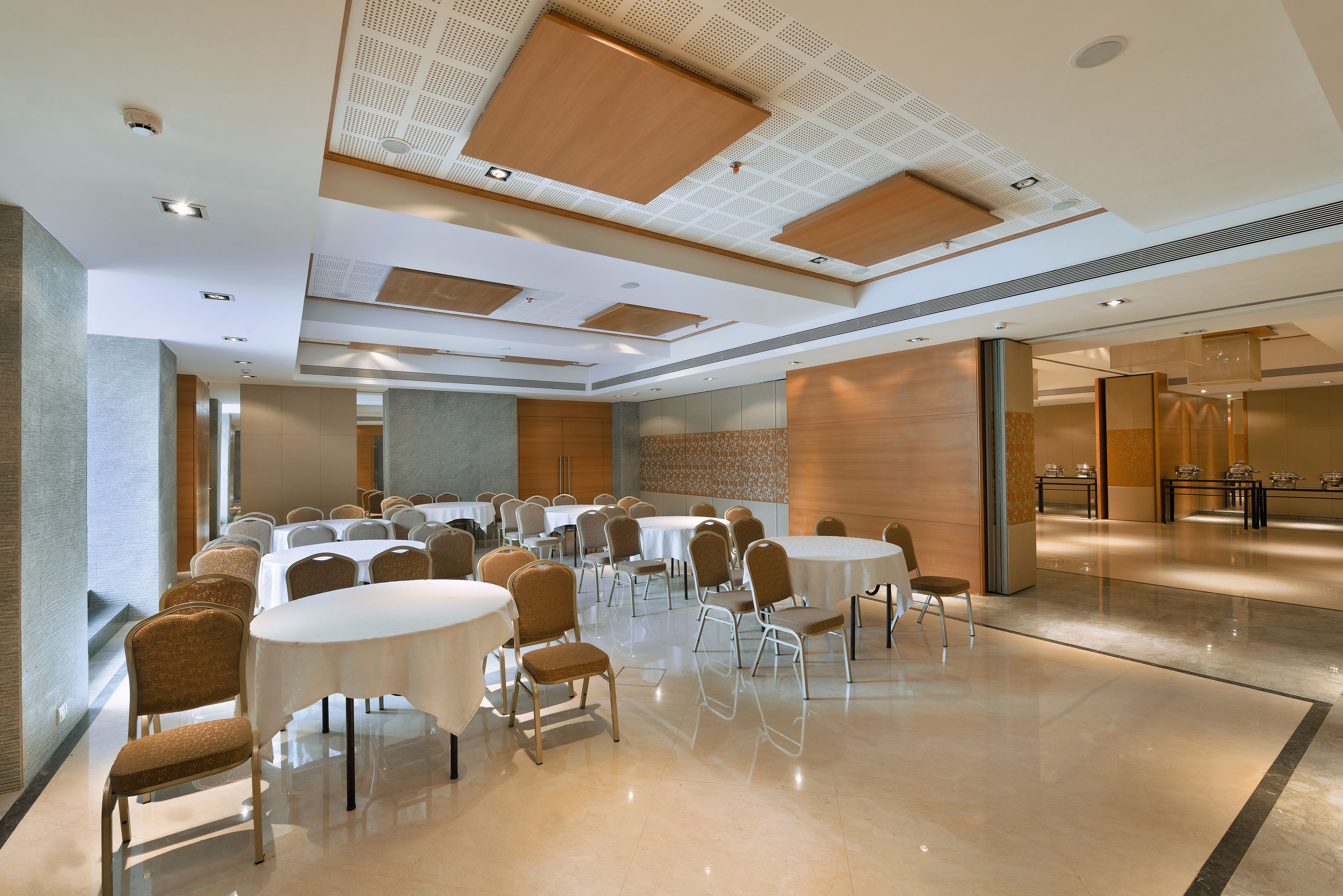 A conference room with multiple tables and chairs, a polished floor, and a modern ceiling design.