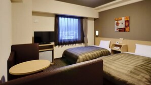 A hotel room with two beds, a desk with a TV, a small round table, and a window with curtains.