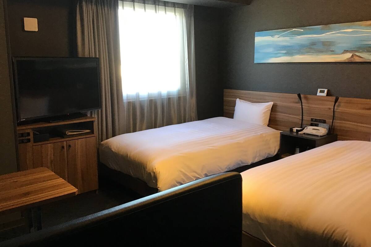 A hotel room with two beds, a TV, a desk, and a painting on the wall.