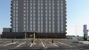 A multi-story hotel with a modern facade, a large parking lot, and a clear sky.