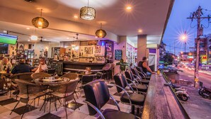 A restaurant with wicker chairs and tables, a bar area, and a view of the street with motorcycles parked outside. - Sutus Court 2 (Pattaya)