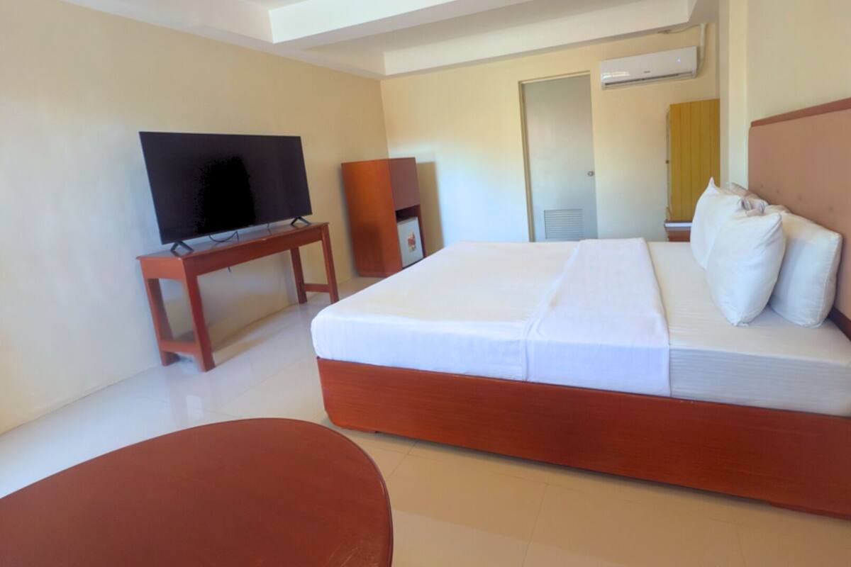 A hotel room with a bed, a television on a stand, a small table, and a chair.