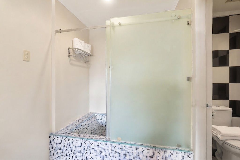 A bathroom with a glass shower enclosure, a tiled shower area, and a toilet visible through the glass.