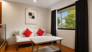 A modern room with a white sofa, two red cushions, a wooden table, and a window with dark curtains. - Whiterock Beach Resort (Subic)