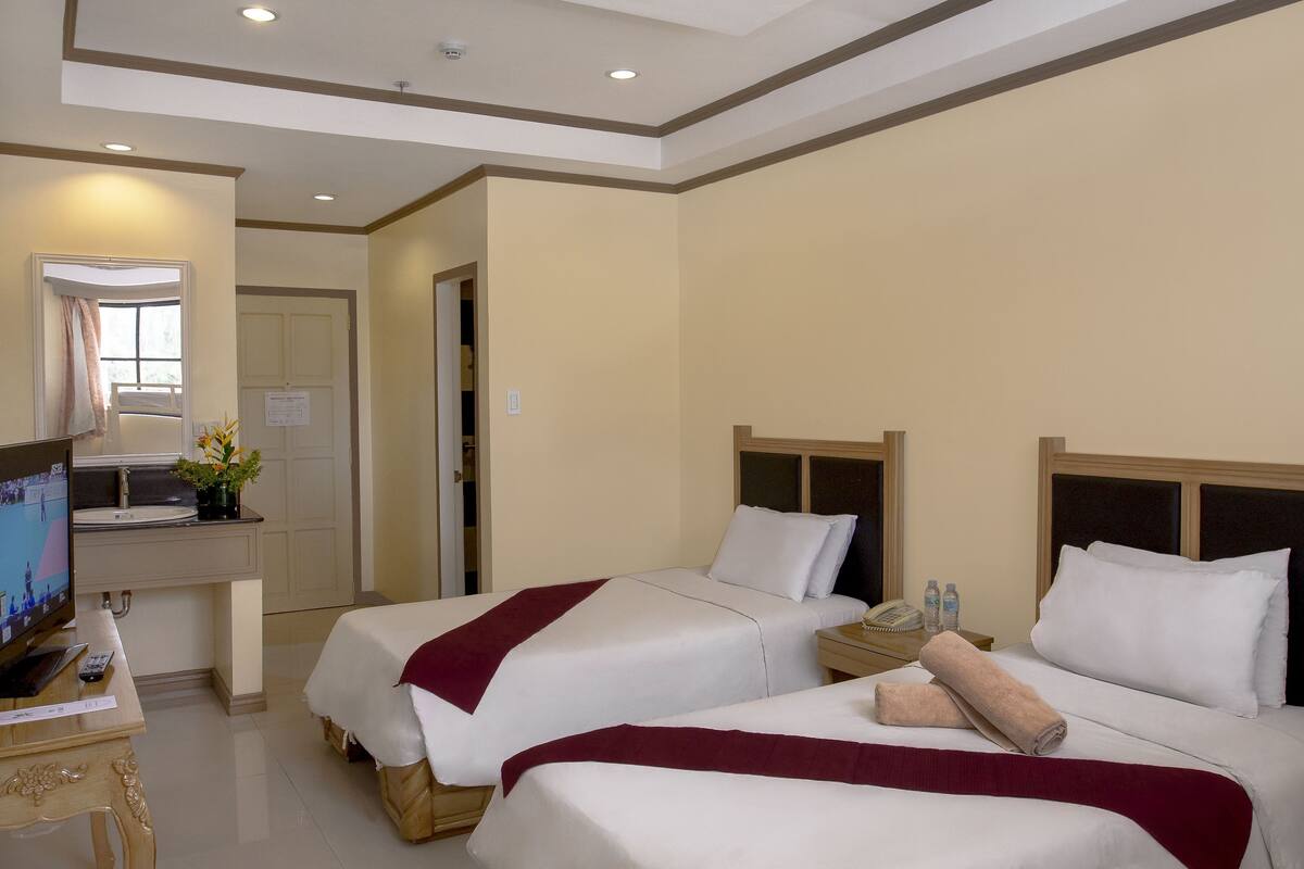 A hotel room with two beds, a desk with a computer, and a mirror.