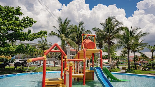 Zona de juegos infantiles con tobogán y estructuras para escalar sobre una piscina.