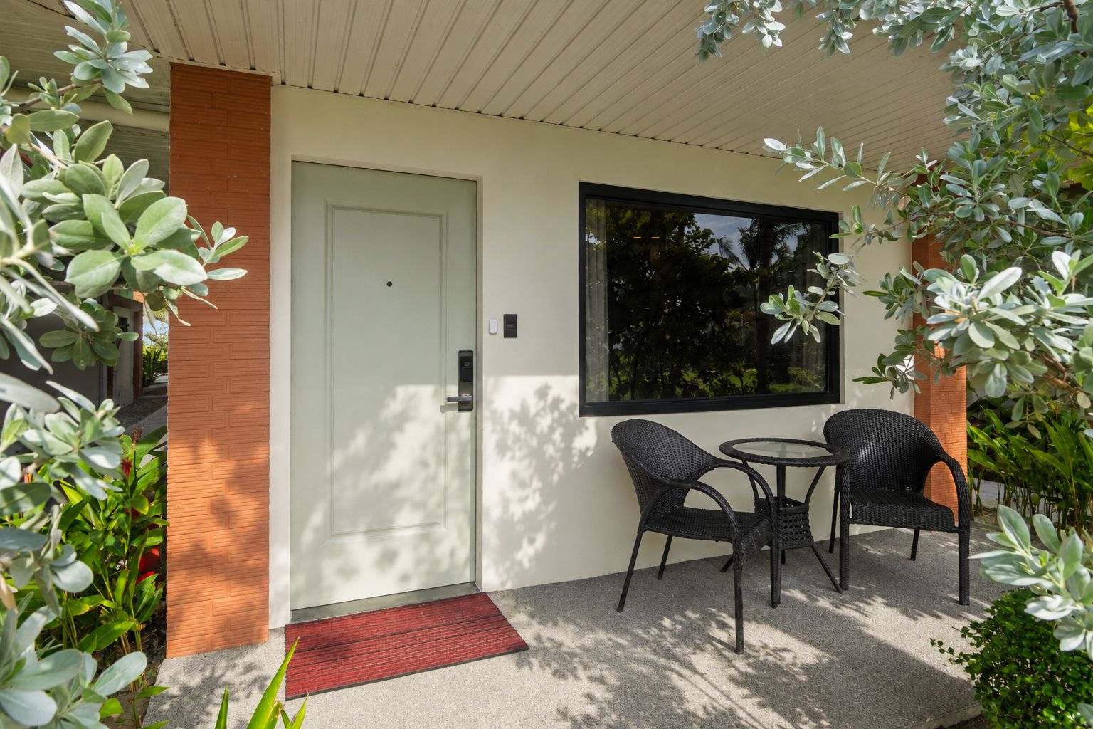 Une façade moderne avec une porte, une fenêtre et un petit espace extérieur aménagé avec deux chaises et une table.