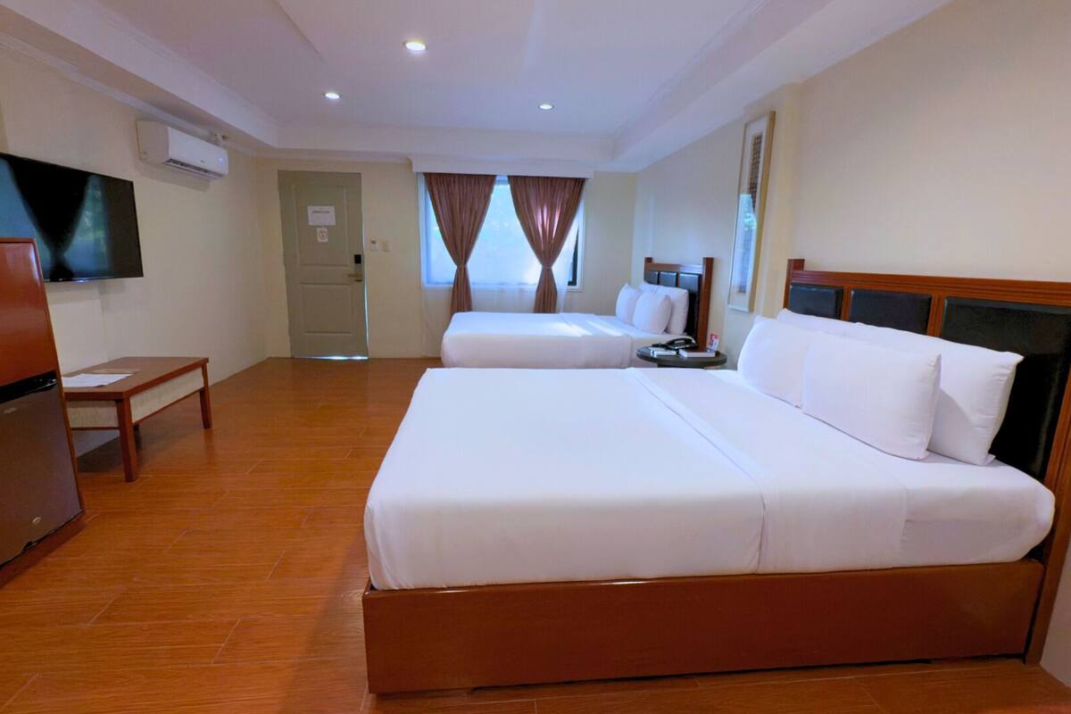 A hotel room with two beds, a television, a refrigerator, and a wooden floor.