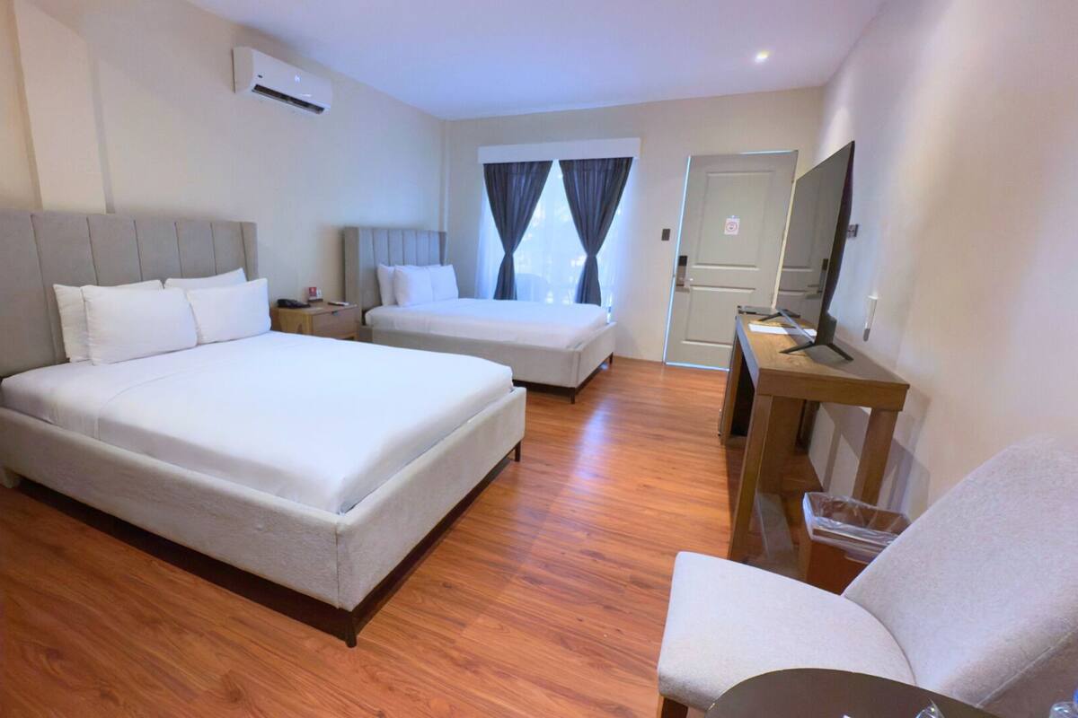 A hotel room with two beds, a desk, a chair, and a TV.