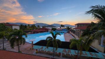 A resort pool area with a view of mountains, palm trees, and a sunset.