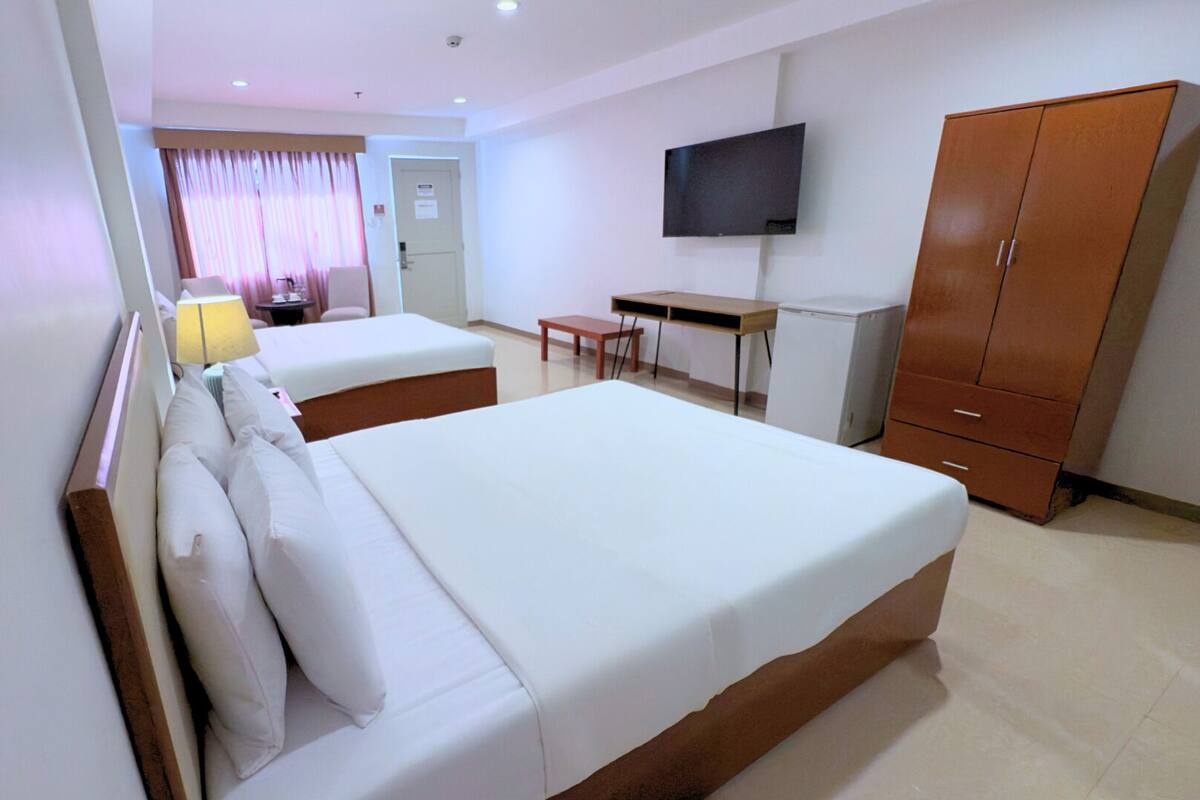 A hotel room with two single beds, a desk, a chair, a TV mounted on the wall, and a wardrobe.