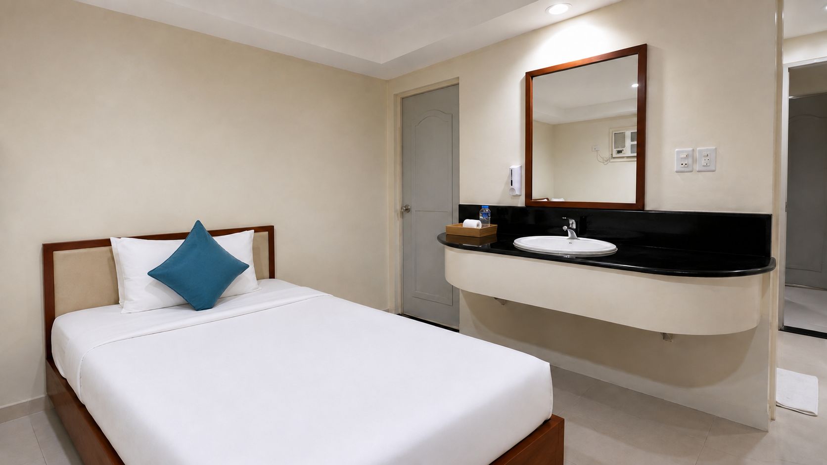 A hotel room with a bed, a bedside table, a mirror, and a bathroom with a sink and mirror.