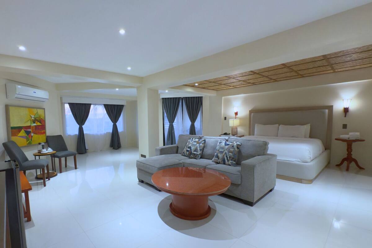 A modern hotel room with a sofa, a round coffee table, a bed, and a TV.