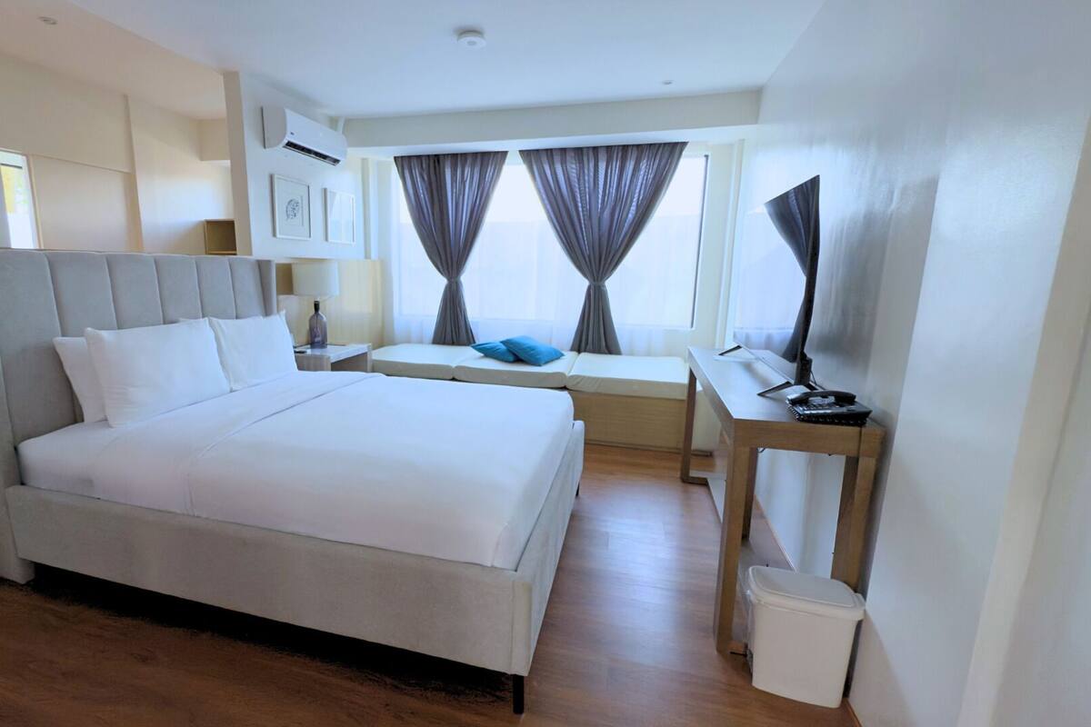 A modern hotel room with a large bed, a desk, and a window with curtains.