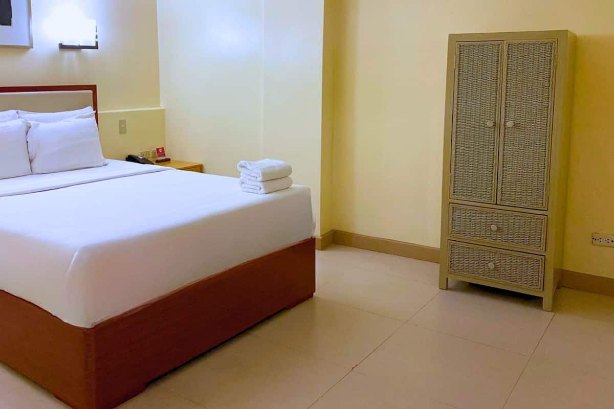 A hotel room with a large bed, a nightstand, a wardrobe, and a wall-mounted light.